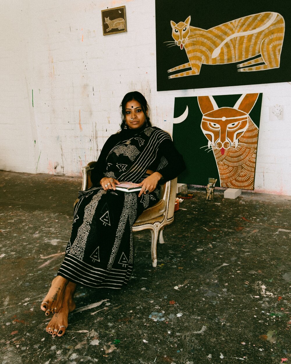Mugdha Martin seated in her studio in front of two Big Cats paintings